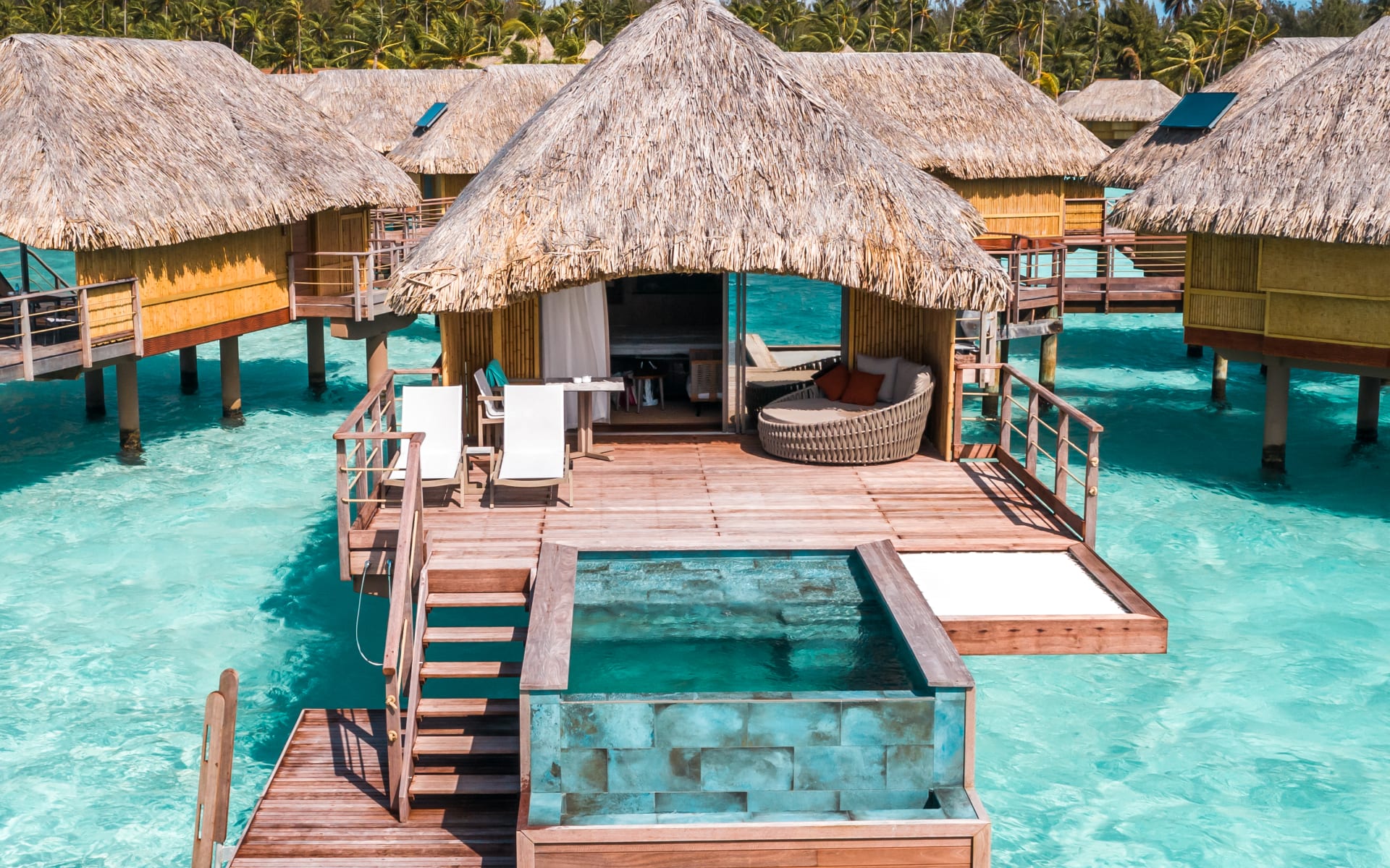An overwater villa has a pool, sun loungers and an outdoor seating area. 
